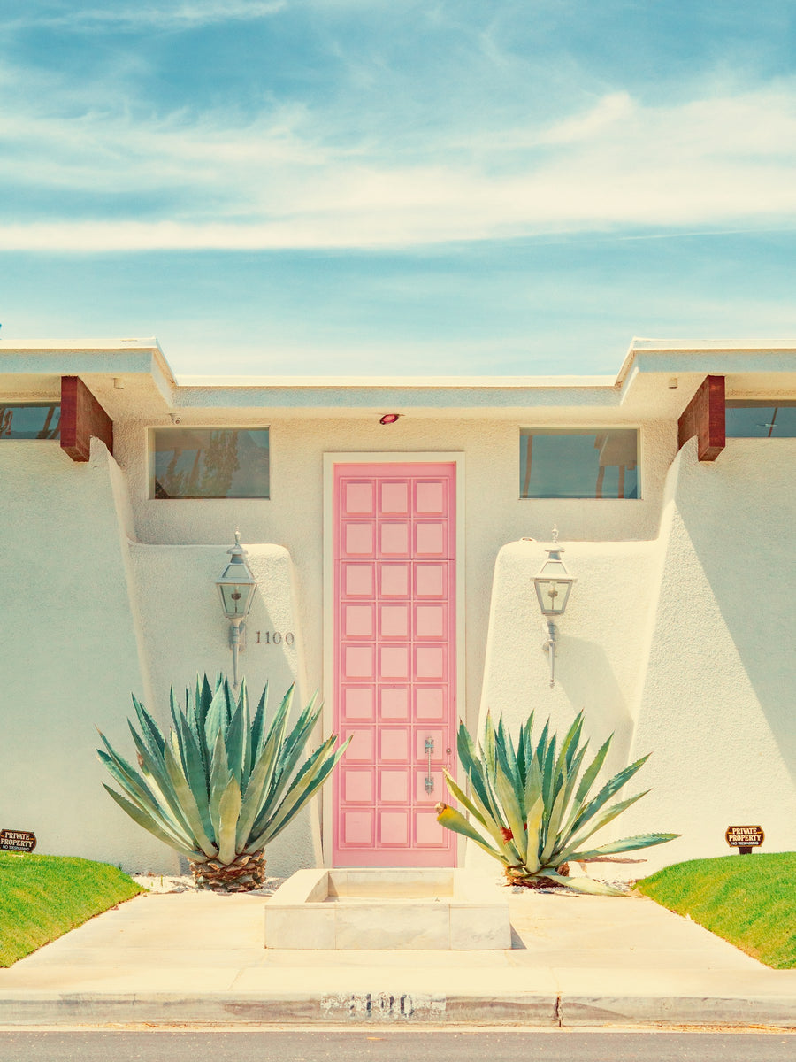 A pink door framed by warm white walls and sculptural green plants