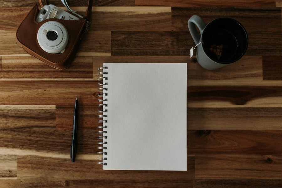 An instant camera, notebook, pencil and tea set out on a wooden table