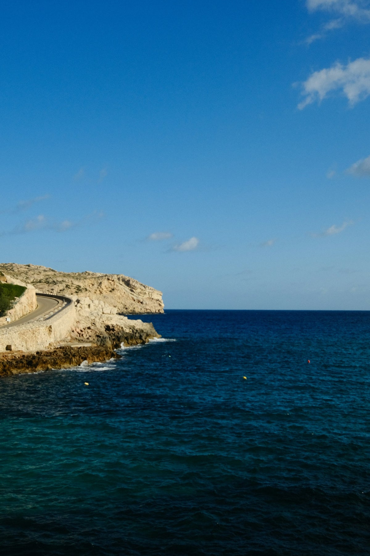 A quiet road following rocky cliffs above a deep blue sea